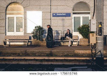 RIOMAGGIORE, ITALY - DECEMBER 2016: Senior man is leaving train station while young man is sitting on a bench near station platform.