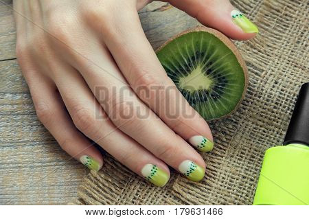 Kiwi, nail polish and skin care of a beauty female hand with green and white moon nail art manicure on a sackcloth and wooden background