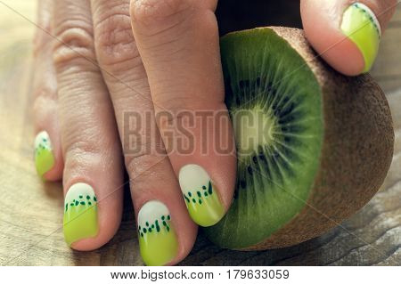 Kiwi and skin care of a beauty female hand with green and white moon nail art manicure on a wooden background