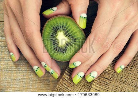 Kiwi and skin care of a beauty female hands with green and white moon nail art manicure on a sackcloth and wooden background