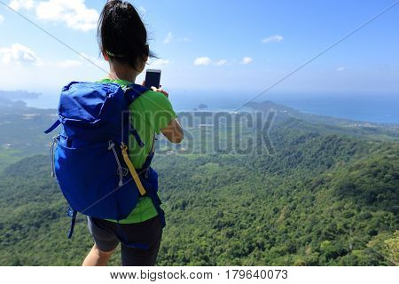 successful woman hiker taking photo with cellphone on mountain top
