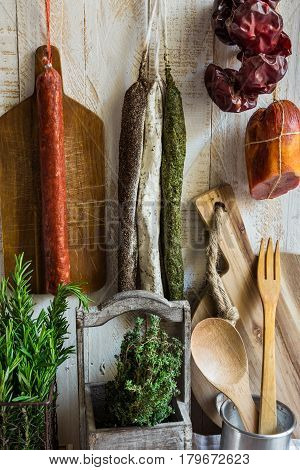 Variety of Spanish cured meat products charcuterie fresh rosemary wood cutting board kitchen utensils hanging on hooks