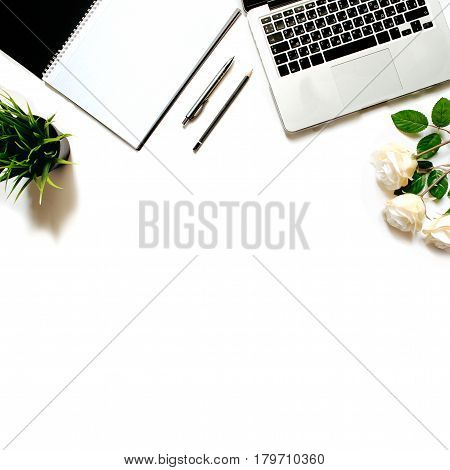 Modern minimalistic work place. White office desk table with laptop keyboard, pen, office plant, white roses. Top view with copy space, flat lay