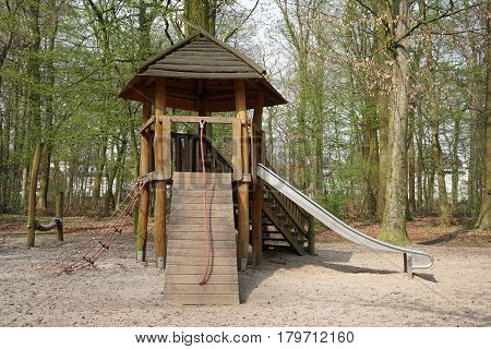 playground in forest with wooden hut, climbing contraption and slide