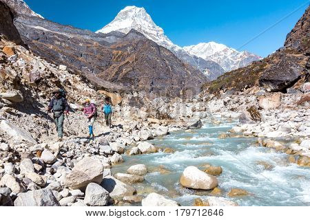People of diverse Ethnicity walking with Backpacks along Mountain River carrying Backpacks warm day