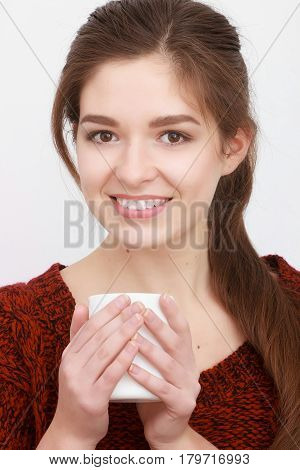 Beautiful girl in red sweater sitting on couch posing and smiling with cup