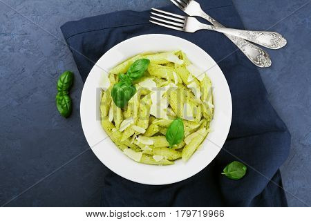 Pasta with pesto sauce decorated basil leaves and parmesan cheese in white plate on blue table top view. Flat lay.