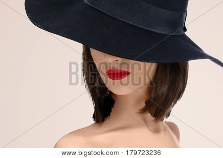 Close up studio portrait of a red lipped woman posing in a hat covering her face mystery mysterious hiding incognito anonymous red lips makeup sexy seductive secret concept .