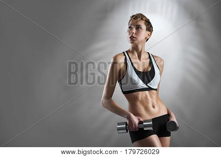 Gym fan. Studio shot of an attractive fit and toned female model holding gym dumbbells looking away thoughtfully on grey background copyspace on the side