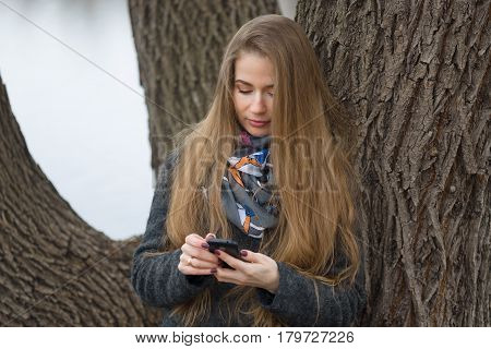 Portrait Of A Beautiful Girl With A Phone In Early Spring Outdoors.