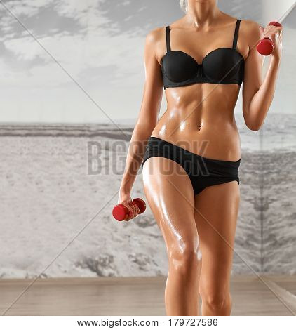 Sexy, athletic, blonde woman in the gym, against the background of the mirror, with dumbbells in hands. Sports, sportswear, health, a beautiful body, body Parts