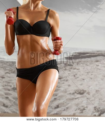 Sexy, athletic, blonde woman in the gym, against the background of the mirror, with dumbbells in hands. Sports, pumped press, a beautiful body, body Parts.