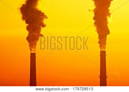 Two industrial pipes with smoke against sunrise or sunset sky. Smog pollution concept and global warming concept