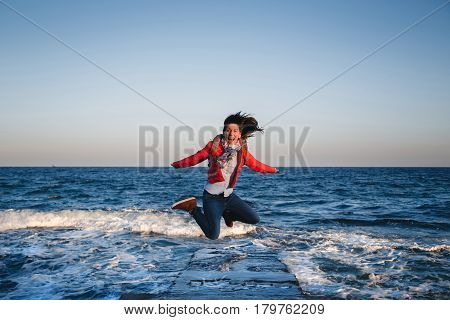 Young happy girl with backpack jumping on a seaside at sunset