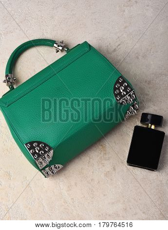 Nice beautiful small womans leather green fashionable bag with decorative metallic spikes or thorns on white textured background near perfume