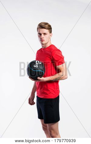 Handsome hipster fitness man in red t-shirt holding medicene ball. Studio shot on gray background.