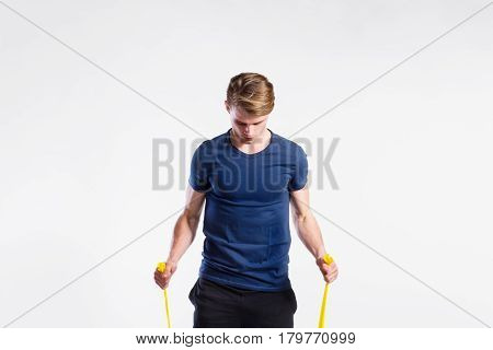 Handsome hipster fitness man in dark blue t-shirt and black shorts working out with resistance bands. Tattoo on his forearms. Studio shot on gray background.