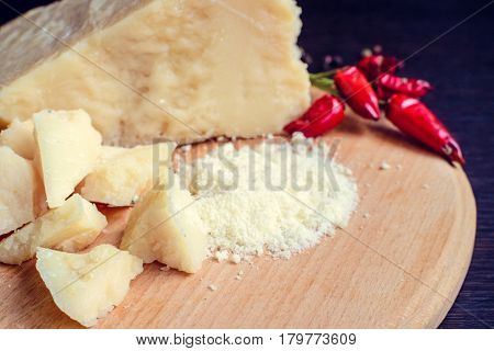 Grated Parmesan cheese with chili pepper on wooden chopping board on dark background. Tasty appetizers. Selective focus.