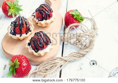 Strawberry cake with vanilla cream on white rusric wooden background. Sweet basket tartlet with strawberries and chocolate. Tasty summer dessert. Selective focus.