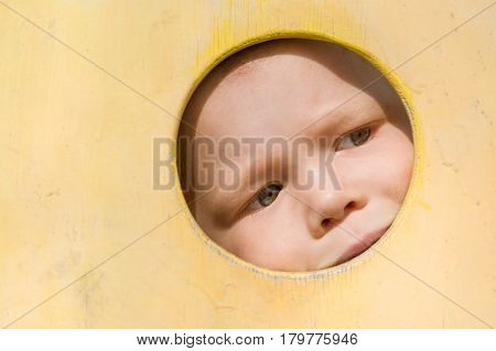 Closeup portrait of cute little toddler boy looking into yellow wooden frame at playground. Curiosity exploration and leaning. Activities for children outdoors. Preschool daycare. Small boy playing