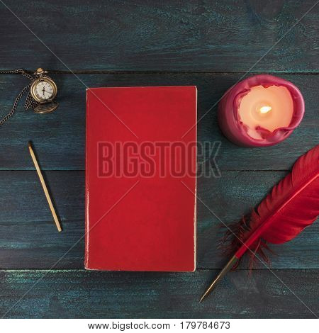 A square mockup with a blank red book cover, a vintage chain watch, a burning candle, a match, and a quill pen