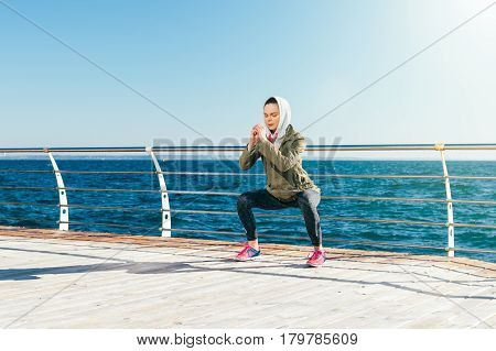 Sports Woman In Hood Doing Exercises On The Coast In The Spring Sunny Morning