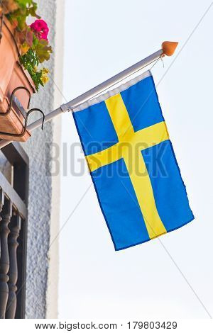Flag of Sweden waving above the balcony of a building, blue sky behind.