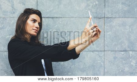 Portrait young businesswomen in black suit using smartphone isolated on background concrete gray wall mockup pretty hipster manager holding mobile gadget girl making selfie photo connect