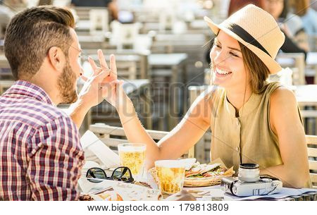 Couple in love having fun at beer bar on travel excursion - Young happy tourists enjoying happy moment at street food restaurant - Relationship concept with focus on girl face on warm bright filter
