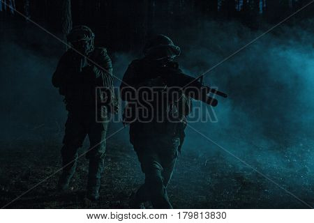 Pair of soldiers in the smoke in action on battle operation. Dark gloomy night, they moving stealthy