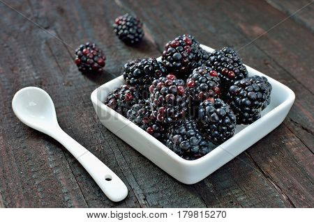Blackberry fruit on wood background. Forest fruit in white idaeus and spoon. Delicious fresh berries.
