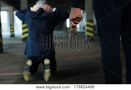 Cold steel. Selective focus of a knife being in hands of a ruthless hardened criminal while kidnapping the businessman