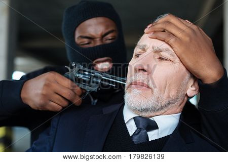 Give me money. Aggressive dangerous male criminal wearing the mask and hiding his face while threatening a businessman with a gun