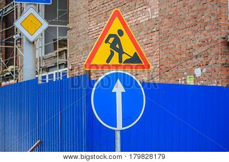 Close up road works and blue go straight signs with main road sign in background