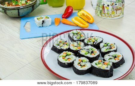Home made vegan sushi rolls on a plate and vegetables on a blue board