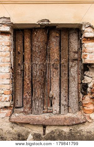 The window of the ruined house closed with wooden boards. The plaster on the wall around the window is crumbled. Masonry is partially destroyed. Very sad scene