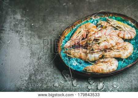 Raw uncooked tiger prawns on chipped ice in turquoise blue ceramic tray over grey concrete background, top view, copy space. Fresh seafood