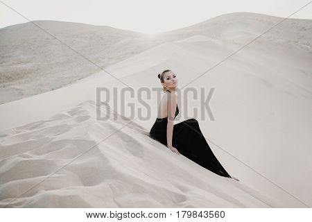 Woman in a black dress is posing in desert