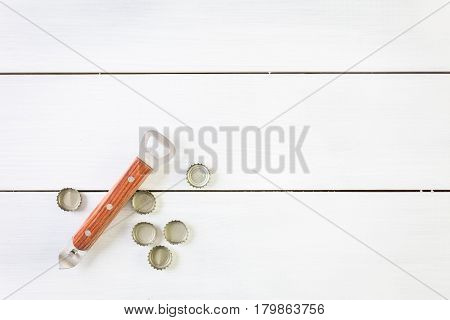 Beer bottle caps and openner on a white wood boards.