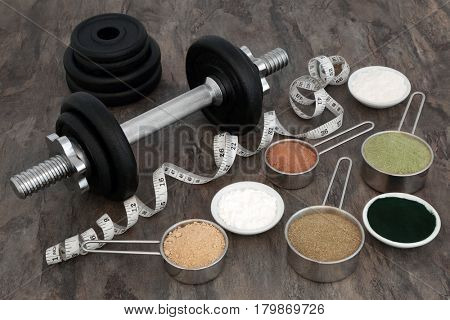 Body building equipment with dumbbell weights, food powder supplements and tape measure over marble background.