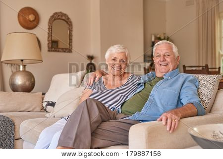 Portrait of a smiling senior man with his arm around his wife's shoulder sitting together on their living room sofa at home