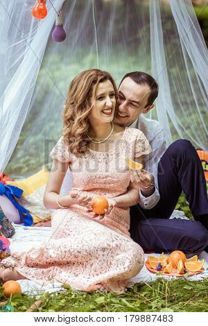 Smiling man and woman sitting on the ground and holdind a piece of orange in Lviv, Ukraine.