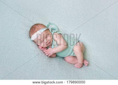 Aborable baby napping oh her side, wearing greenish dress and a flowery hairband