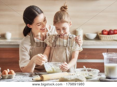 Happy loving family are preparing bakery together. Mother and child daughter girl are cooking cookies and having fun in the kitchen. Homemade food and little helper.