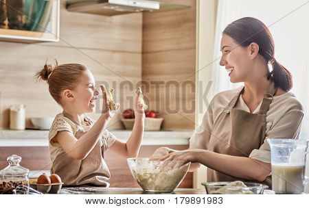 Happy loving family are preparing bakery together. Mother and child daughter girl are cooking cookies and having fun in the kitchen. Homemade food and little helper.