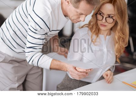 Feeling abuse at work. Handsome confident aging businessman standing in the office and working on the project while flirting and touching young secretary hand