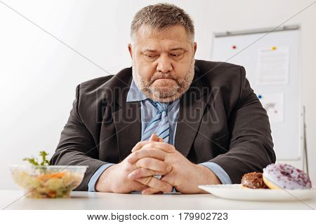 Hard choice to make. Immoderate unhealthy puffy guy thinking about changing his diet for taking care of himself
