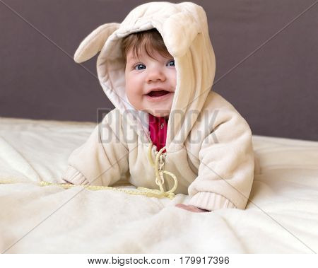 Little Beautiful Baby In A Funny Costume With Ears Laughs, Lying On His Stomach.