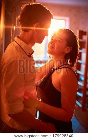 Young people hugging in the apartment in the evening in the rays of the sunset. A loving couple on a date on a summer evening. The guy with the girl hugs and kisses. Youth, first feelings, first love, first dates. faces close up. Sun flares in the frame a