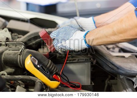car service, repair, maintenance and people concept - auto mechanic man with digital multimeter testing battery at workshop
